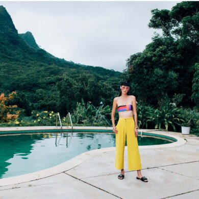 model in luxury fashion sports yellow pants and a cropped tube top against a pool background