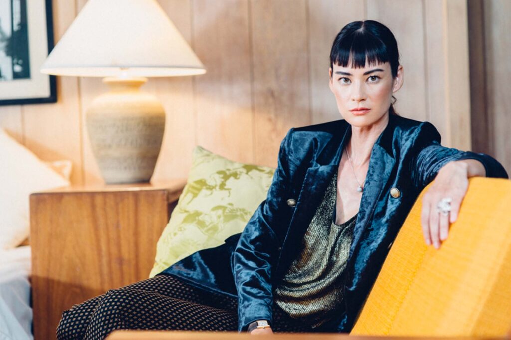 model wears a velvet jacket with a scoop neck top lounging on a modern couch in a cool environment. 