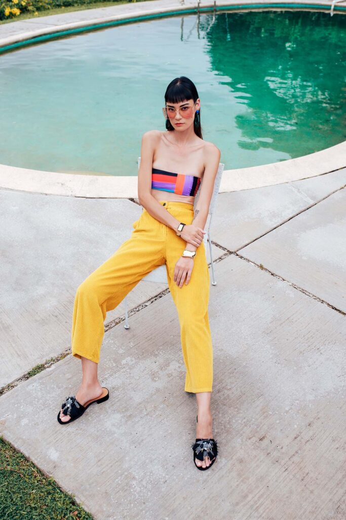 young model in bold yellow pants and tube top casually by the pool