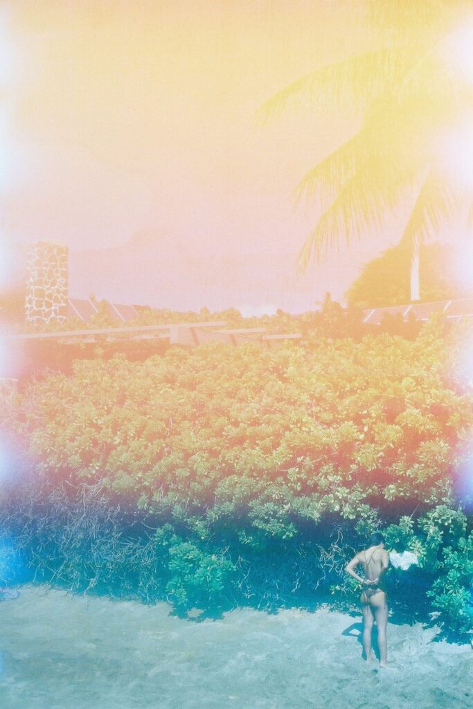 pastel rainbow filter of a woman in bikini standing against greenery and the sand